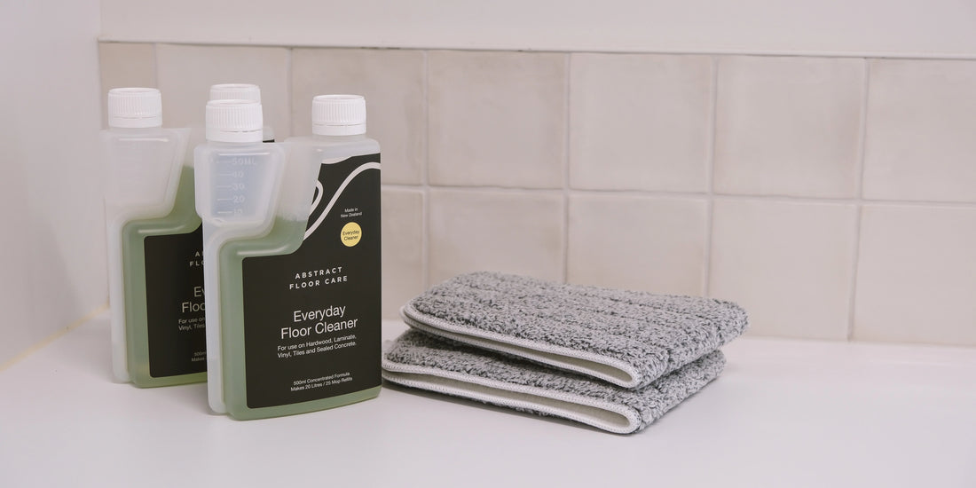 Bottle of pH-neutral laminate floor cleaner beside a spray mop on clean, streak-free laminate flooring