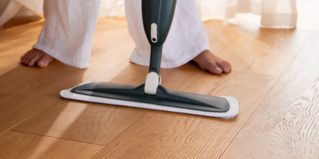 Person using a spray mop with microfibre pad to clean shiny laminate wood floors in a bright modern home