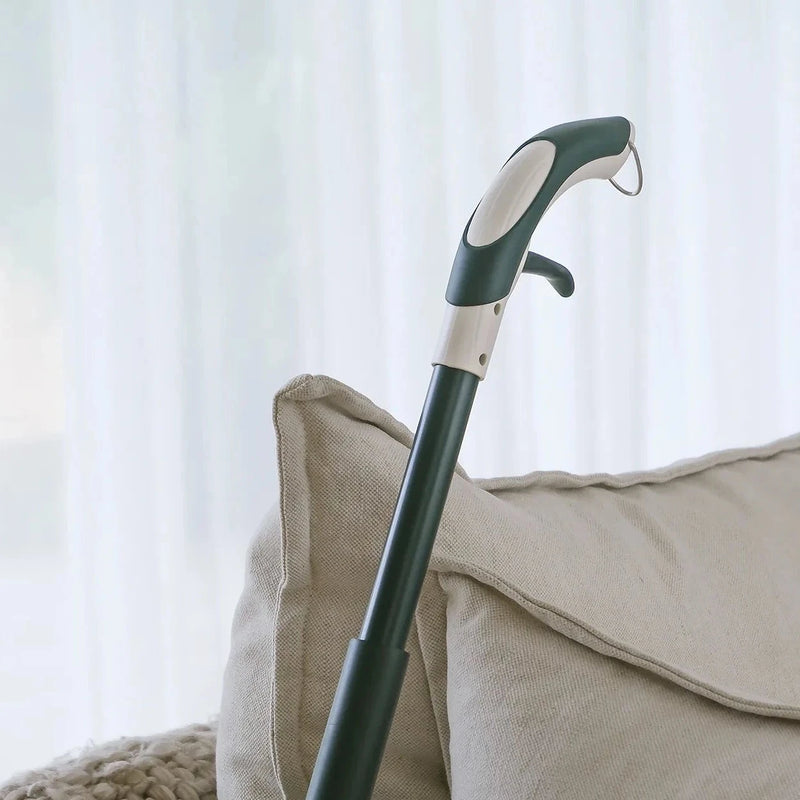 Black and white mop handle leaning against a beige sofa with light curtains in the background