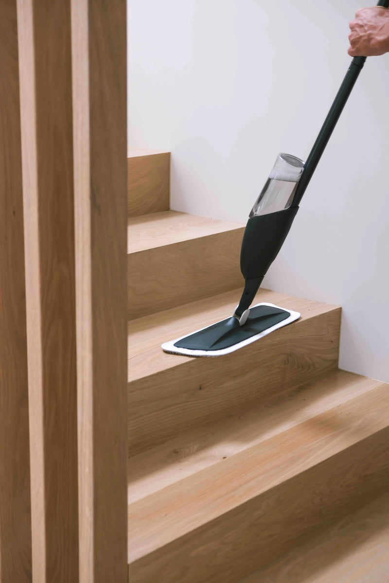 Person cleaning wooden stairs with a grey and dark green mop. 