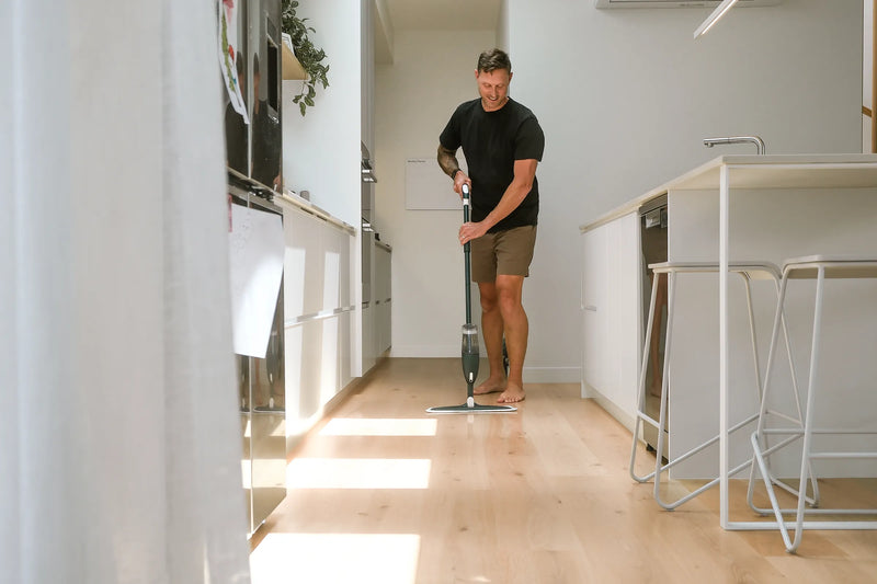 Man cleaning a modern kitchen floor with a mop.