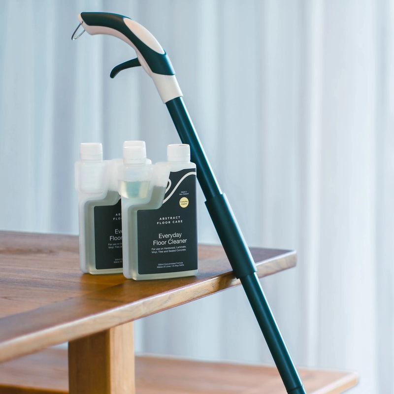 Cleaning mop and bottles on a wooden table with a white curtain background